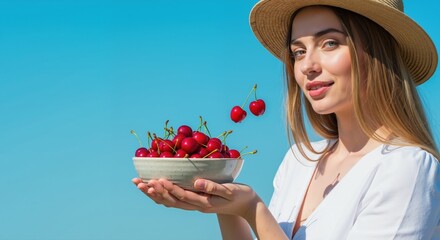 Young woman smiling while holding bowl of cherries against blue sky  