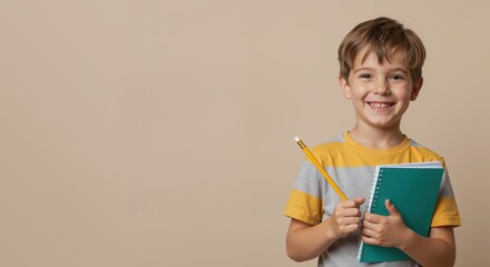 Young boy smiling while holding a notebook and pencil indoors  