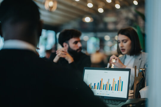 Multicultural businesspeople collaborating and analyzing sales data in a dynamic workplace environment. Visible are charts on a laptop, illustrating data driven discussions and productive teamwork.