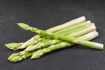 Bunch of raw fresh green asparagus stalks on black, gray textured background. Healthy food, fresh...