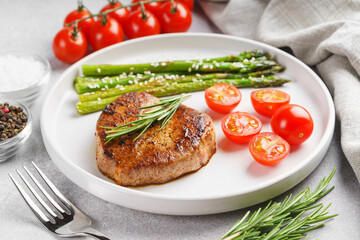 Close up, macro of tasty grilled beef steak served with green asparagus and cherry tomatoes on white plate, with cutlery. Perfect for food menu, diet, or culinary design concepts.
