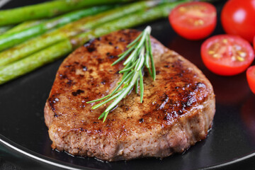 Close up, macro of tasty grilled beef steak served with green asparagus and cherry tomatoes on black plate, with cutlery. Perfect for food menu, diet, or culinary design concepts.