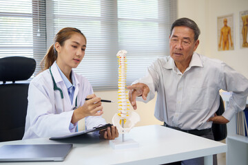 Doctor explaining spine anatomy using model during consultation with elderly patient concerned...