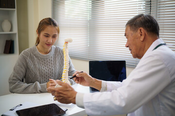 Senior male doctor explaining spine anatomy to a young woman using a medical model in a clinical.