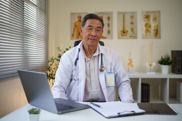 Fototapeta premium Senior male doctor using a laptop to review patient records in a modern clinic.
