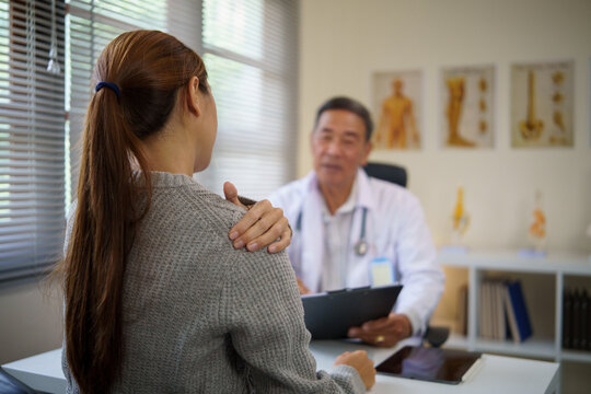 Female patient describing shoulder pain while consulting with a senior doctor in a clinic. Health care concept.