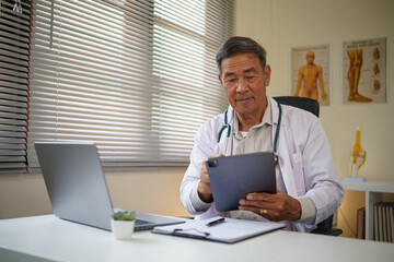 Fototapeta premium Experienced physician using technology to update patient records at his desk.