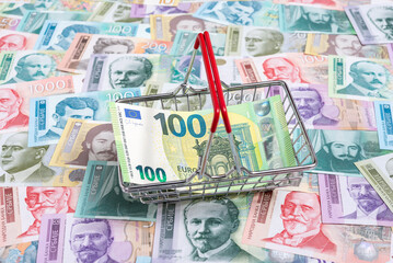 Shopping basket with a 100 euro bill on a pile of Serbian paper money