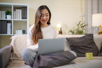 Young woman relaxing on a couch and using a laptop, working comfortably from her living room.