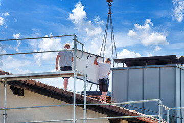 Two roofers dismantle solar panels and prepare them for crane transport