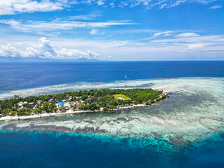 Picturesque Tropical Island with Village and Jetty Surrounded by Clear Blue Waters and Coral Reefs in Indonesia