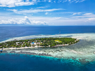 Fototapeta premium Picturesque Tropical Island with Village and Jetty Surrounded by Clear Blue Waters and Coral Reefs in Indonesia
