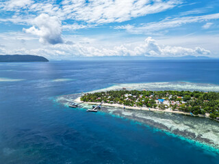 Obraz premium Picturesque Tropical Island with Village and Jetty Surrounded by Clear Blue Waters and Coral Reefs in Indonesia