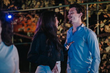A couple engaged in joyful conversation at an outdoor evening event, illuminated by soft lighting. The festive atmosphere showcases celebratory and social vibes, highlighting interpersonal connections