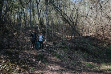 Obraz premium A man and woman venture through a wooded area, equipped with backpacks and walking poles, on a serene hiking excursion to connect with nature.