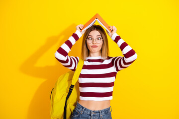 Stylish young woman with a striped sweater and yellow background, playfully posing with a book on...