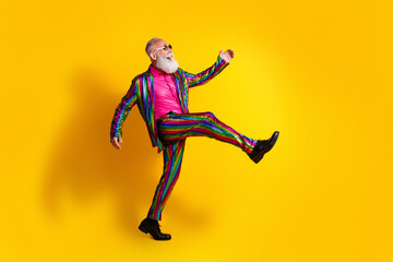 Elderly man in a funky striped suit kicks energetically against vibrant yellow background