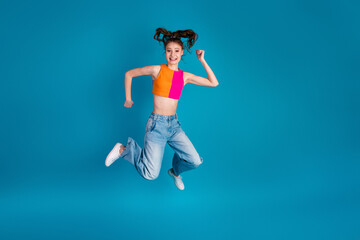 Excited young girl jumps high in casual attire against a vibrant blue background showcasing fun and...