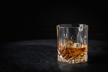 Whiskey with ice in glass on dark background, copy space