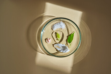 Various cosmetics in a petri dish on a beige background.