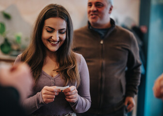 A cheerful woman reading a slip of paper while socializing with a group of people. The atmosphere is informal, engaging, and warm, capturing a sense of community and goodwill.