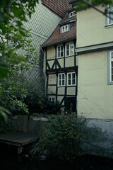 Charming old half-timbered house with black wooden beams and white plaster, surrounded by greenery and located next to a small stream in Wolfenbüttel, Germany.
