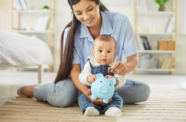 Portrait of happy family of mother and little cute baby putting money coin into piggy bank sitting...