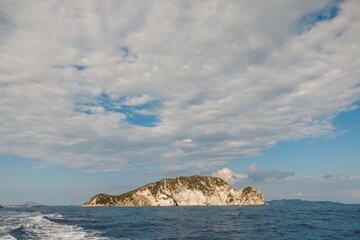 An enchanting island emerges from calm waters, framed by an expansive sky filled with fluffy...