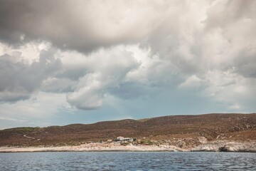A remote island reveals a quaint coastal settlement nestled against rolling hills, as dark clouds...