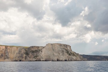 Towering cliffs dominate the horizon, surrounded by calm seas and a dramatic sky filled with...