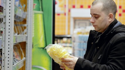 Male shopper reading snack bag label, comparing nutritional information and making mindful grocery...