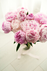 Bouquet of Fresh Pink Peonies with Green Leaves on a Light Background