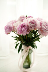 Fresh bouquet of pink peonies in a glass vase with ribbon