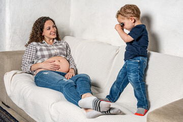 Curious son looking closely with binoculars at his mom’s pregnancy
An infant wants to know what sibling will come out of her mother.