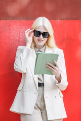 Albino businesswoman in cream suit works on a tablet against a red wall