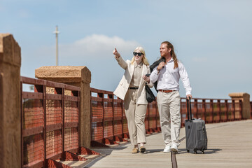 Albino woman and redhead man traveling together on a bridge with luggage and pointing © Juan Algar