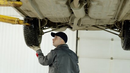 Professional mechanic checking vehicle undercarriage while wearing protective gloves, performing...