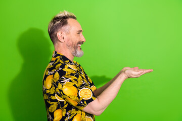 Cheerful mature man with dyed blonde hair presenting with hands against vibrant green background in...