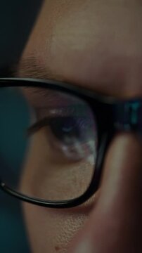 Close-up view of concentrated eyes behind glasses, fixated on a brightly lit computer screen at night. The individual is immersed in digital work or exploration, highlighting dedication