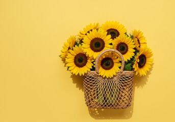 A basket filled with bright yellow sunflowers against a solid yellow background creating a vibrant...