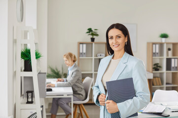 Professional businessewoman dressed in formal clothing posing with notepad in office environment...