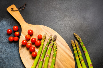 Fresh asparagus and cherry tomatoes arranged on a wooden cutting board for healthy meal preparation