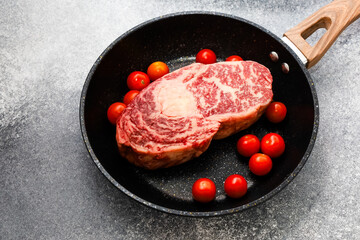 Fresh marbled steak and cherry tomatoes in a frying pan ready for cooking at home