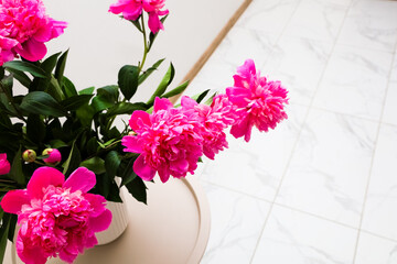 Bright pink peonies in a vase on a light tile surface adding color to a room