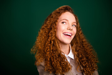 Young businesswoman with curly red hair smiling confidently against an emerald green backdrop in...