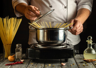 A chef pours uncooked spaghetti into a boiling pot on the stove, surrounded by fresh ingredients...