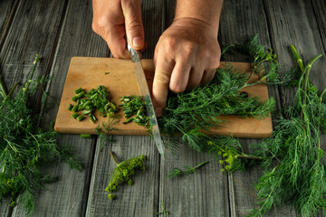 A person finely chops green herbs on a wooden board, surrounded by freshly picked greenery. Natural...