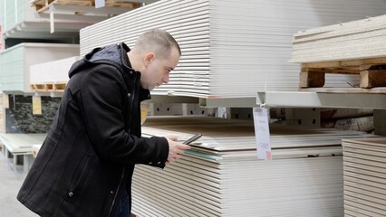 Warehouse customer comparing plasterboard prices on smartphone while walking through hardware store...