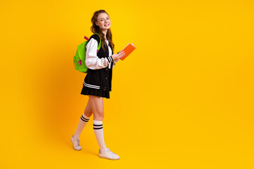 Young female student holding a book smiling confidently against a vibrant yellow background...