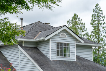 Top of grey stucco luxury house with shingle roof, green trees and nice windows in Spring in Vancouver, Canada, North America. Day time on May 2025.